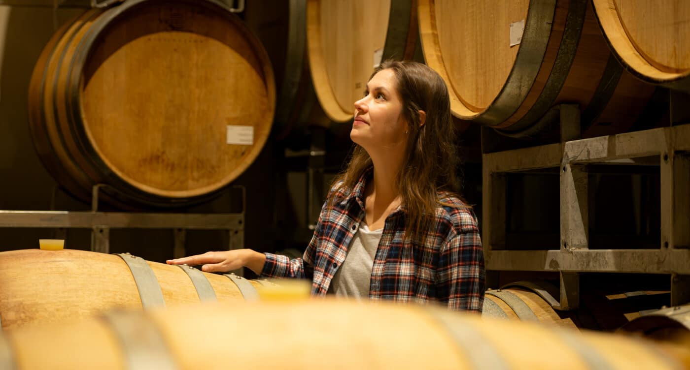 Portrait of a young woman surrounded by wine barrels In her winery