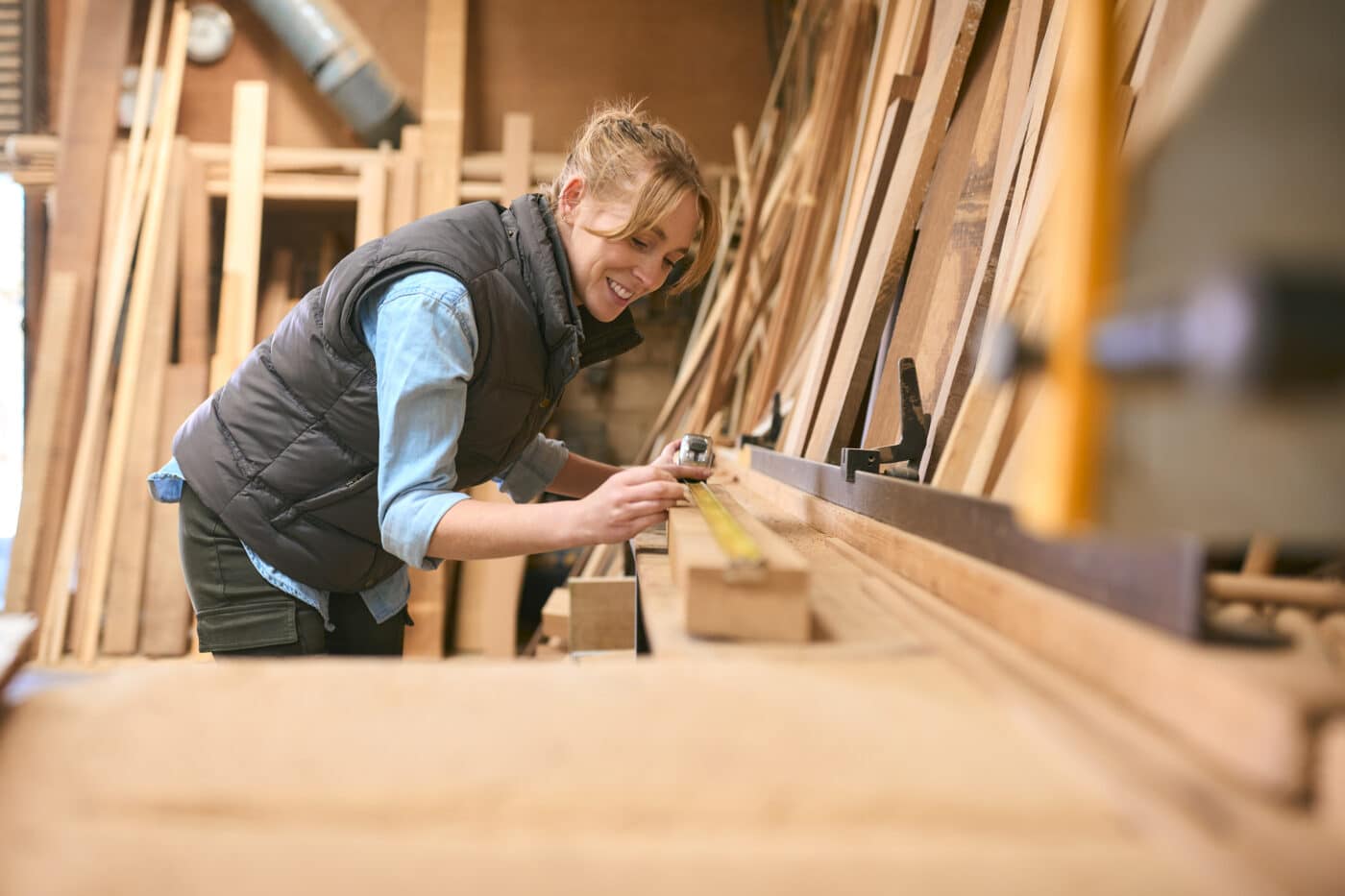 Female Carpenter Working In Woodwork Workshop Measuring Wood For Project